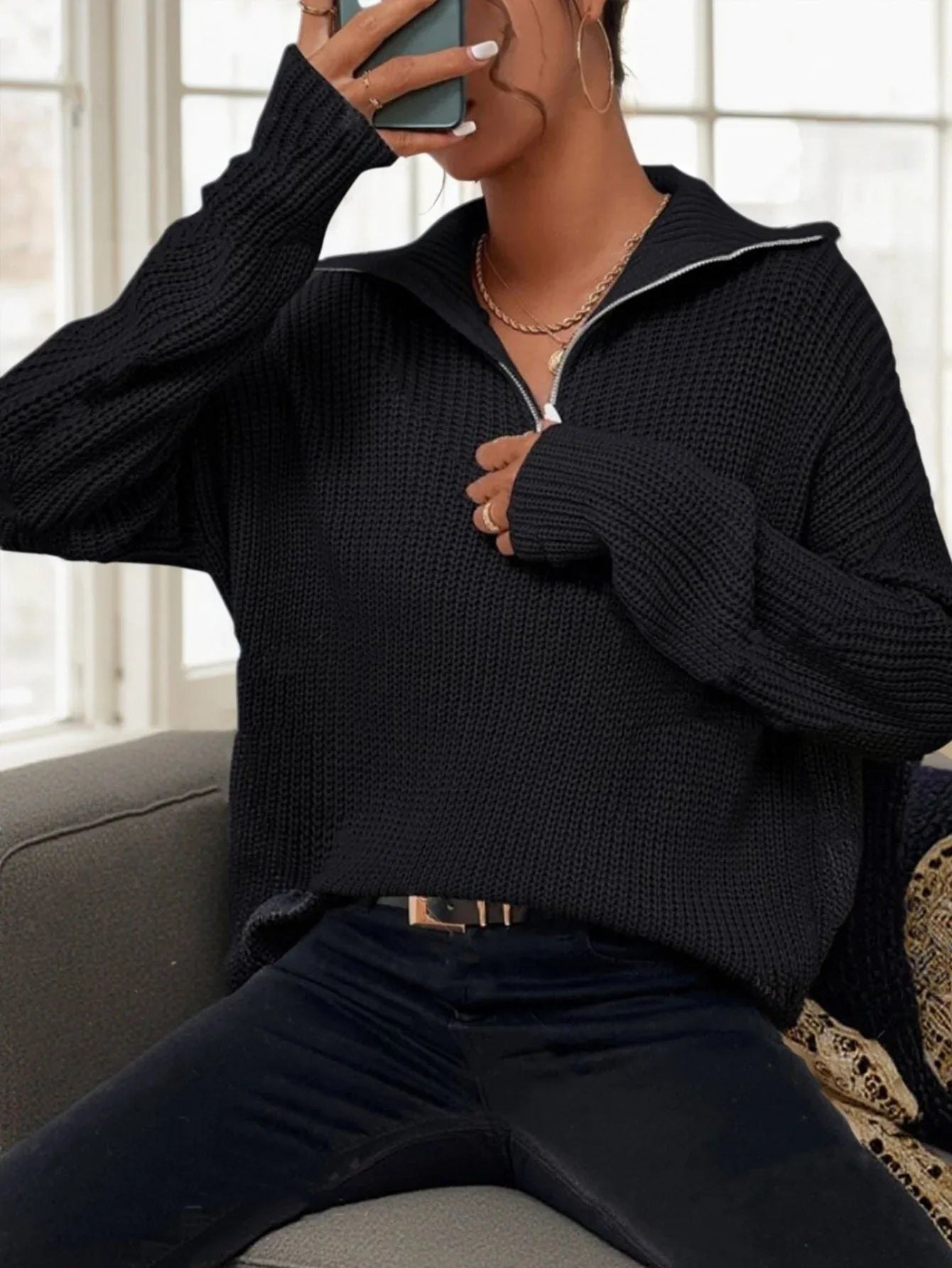 Woman sitting on a couch wearing a black ribbed knit sweater.