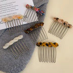 Assortment of marbled resin twisted hair combs with metal teeth scattered on a grey garment