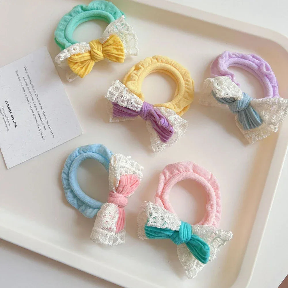 Various pastel scrunchies with bows and lace trim arranged on a white tray