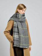 Woman in a tan coat with her large houndstooth and plaid scarf loosely draped