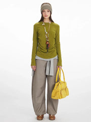 Woman wearing a green long-sleeved top, grey layered knit, taupe wide-leg pants, and carrying a yellow handbag.