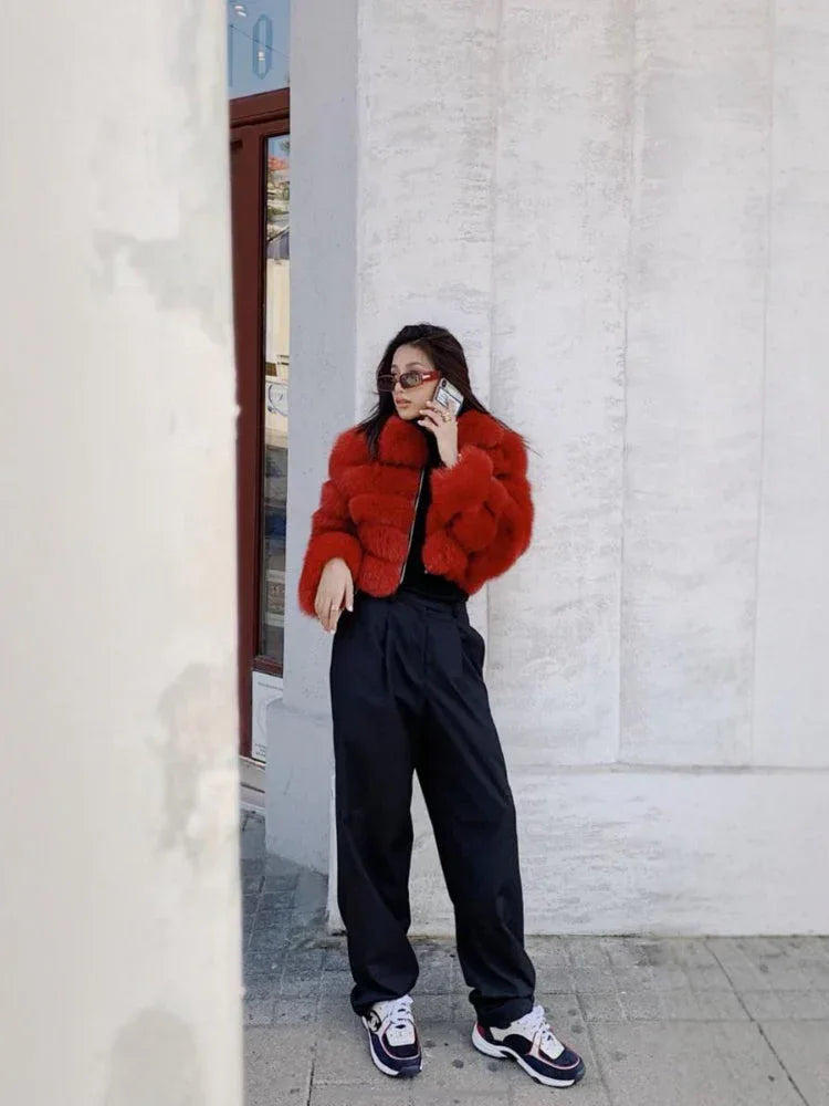 Woman wearing a red fur jacket and black pants talking on the phone