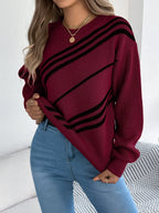 Woman showing the hem of a burgundy knit sweater with black diagonal stripes, blue jeans, and gold rings.