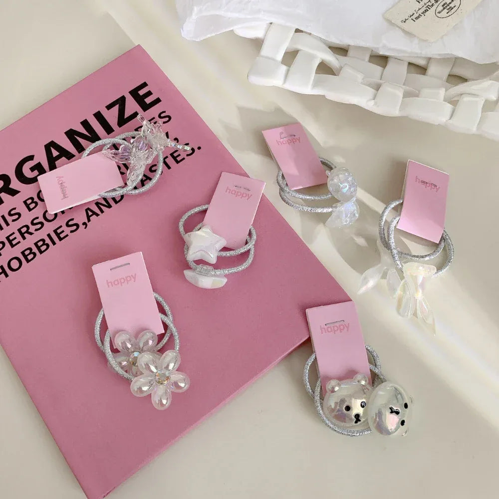 Several charming hair ties with pink 'happy' tags are scattered on a pink surface and white crumpled paper.