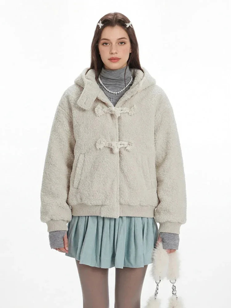 Close-up of a cream fuzzy hooded bomber jacket with toggle closure, worn over a grey turtleneck and a light blue pleated skirt.