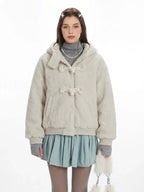 Close-up of a cream fuzzy hooded bomber jacket with toggle closure, worn over a grey turtleneck and a light blue pleated skirt.