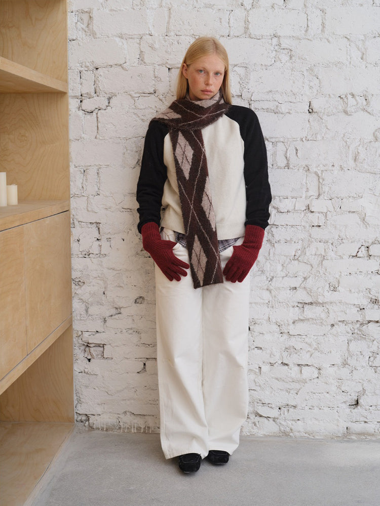 Model wearing a cream and black sweater with an argyle scarf and white pants