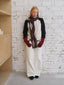 Model wearing a cream and black sweater with an argyle scarf and white pants