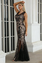 Woman posing in a black and gold sequin evening gown with a thigh-high slit.