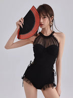 Woman in a black one-piece swimsuit with a sheer halter neckline, holding a red and black fan