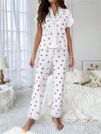 Woman wearing white short-sleeve pajama top with cherry print and white ribbed pants with cherry print, standing in a bedroom.