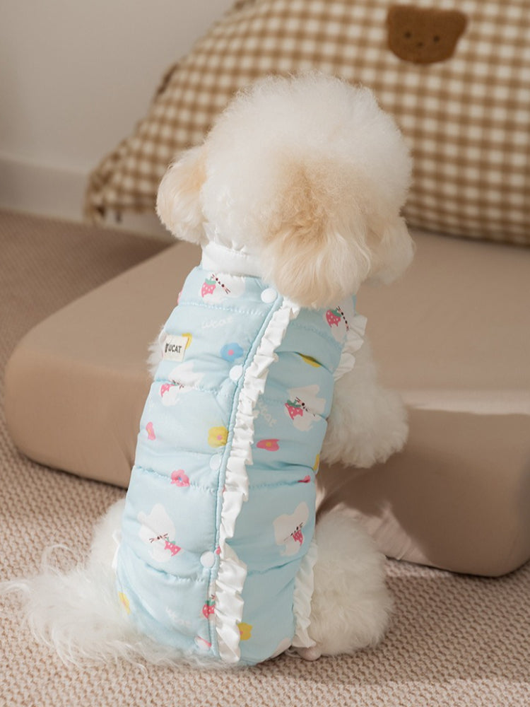 View from the back of a white poodle wearing a light blue pet vest with a strawberry and cloud print and ruffle trim.