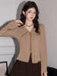 Woman wearing a tan ribbed knit long-sleeve top with a tie-front closure and ruffled hem, paired with a brown pleated skirt.