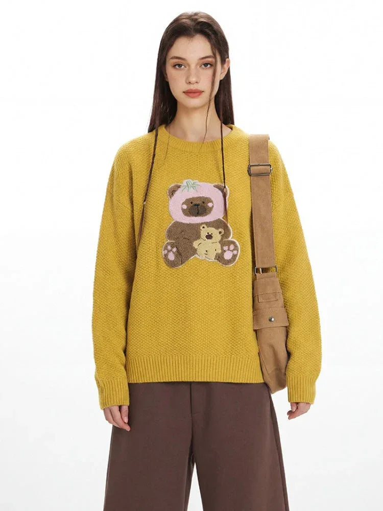 Close-up of a woman wearing a yellow crew neck sweater with an embroidered bear graphic.