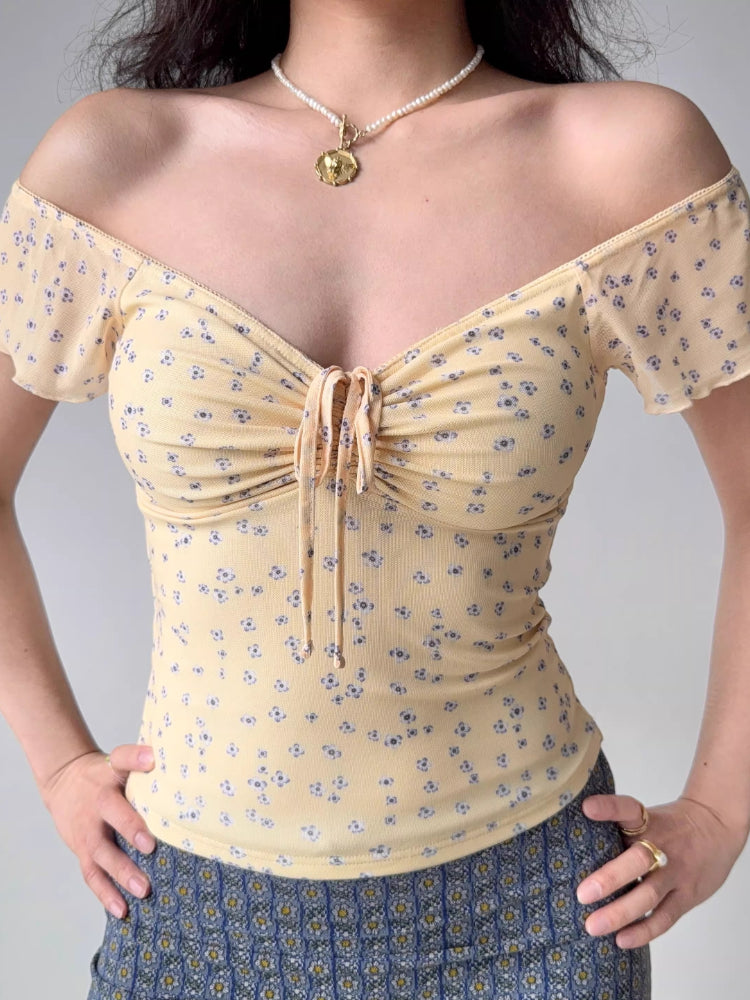 Woman wearing a yellow floral print mesh top with a sweetheart neckline and ruched tie front.