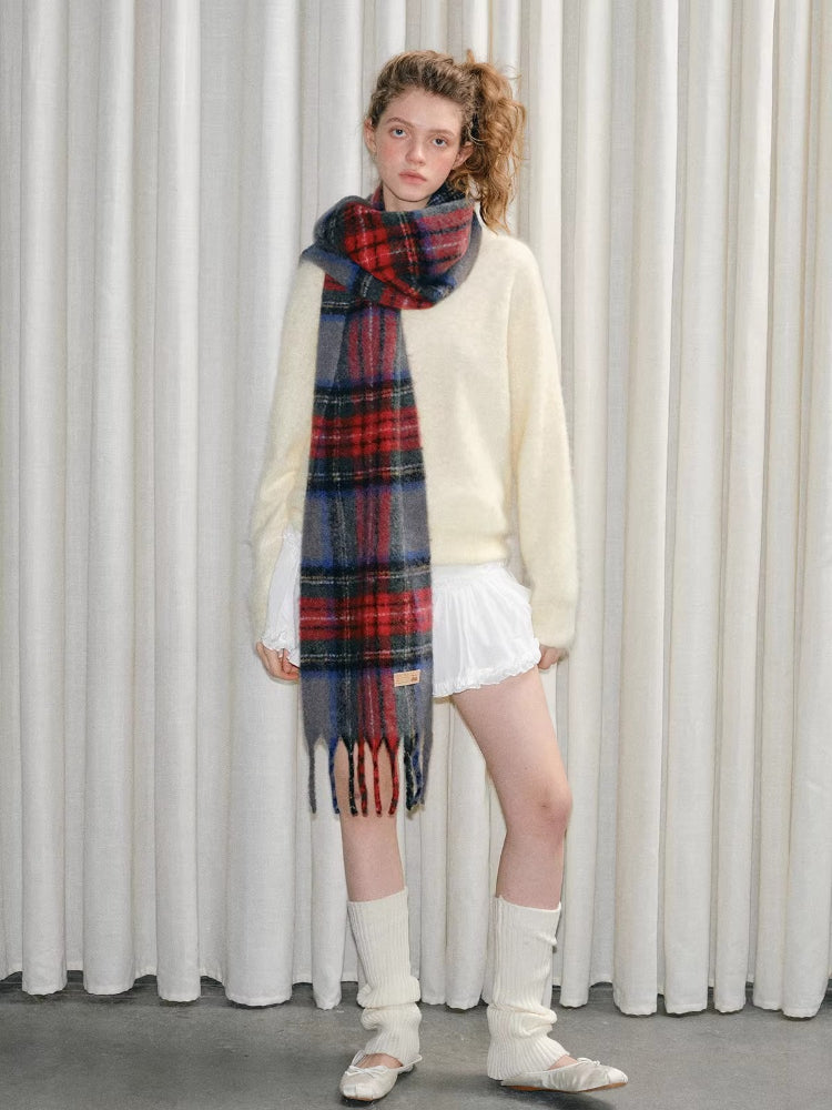 A young woman modeling a cream-colored fuzzy sweater, a red, blue, and gray tartan plaid scarf, and white socks with ballet flats.