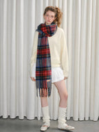 A young woman modeling a cream-colored fuzzy sweater, a red, blue, and gray tartan plaid scarf, and white socks with ballet flats.