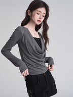 Model adjusting the grey long-sleeved top with a draped neckline.