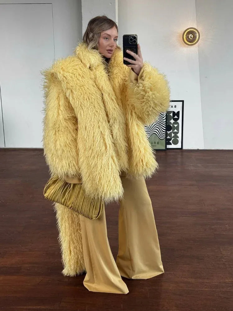 Woman wearing a yellow shaggy faux fur oversized jacket with matching yellow wide-leg pants and a gold clutch.