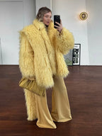 Woman wearing a yellow shaggy faux fur oversized jacket with matching yellow wide-leg pants and a gold clutch.