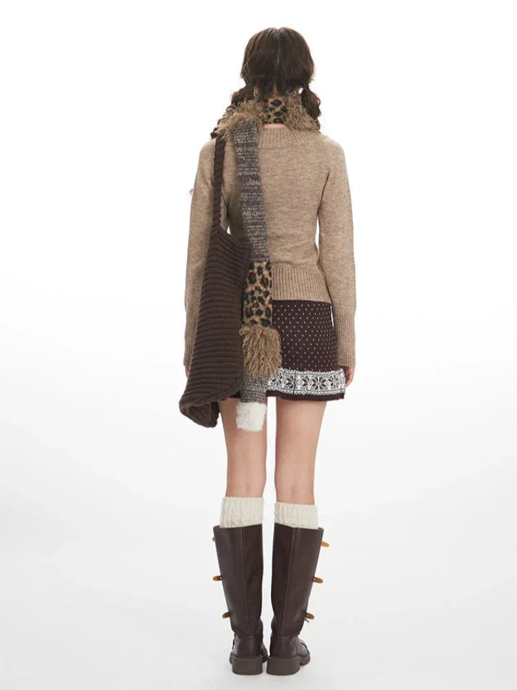 Back view of a woman wearing a beige V-neck sweater, brown patterned mini skirt, white thigh-high socks, and brown boots. Secondary image