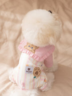 Rear view of a white dog in a pink and yellow striped jumpsuit with a bear face appliqué.