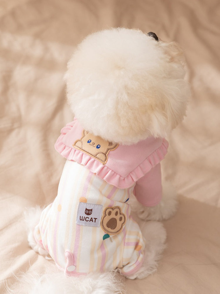 Rear view of a white dog in a pink and yellow striped jumpsuit with a bear face appliqué.