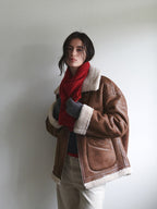 A woman wearing a brown aviator jacket and a red scarf, adjusting her scarf.