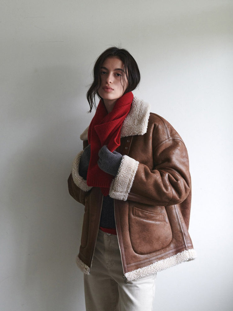 A woman wearing a brown aviator jacket and a red scarf, adjusting her scarf.