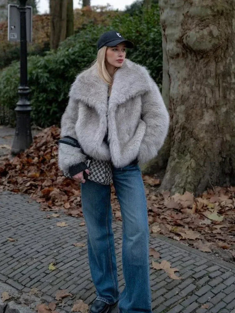 Woman wearing a light grey oversized faux fur jacket with a black baseball cap and blue jeans Main image