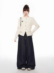 Full body shot of a woman wearing a cream cable knit cardigan and dark wide-leg jeans, standing with one hand on hip