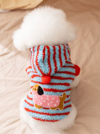 A white Bichon Frise dog wearing a blue and red striped hooded dog coat with a dachshund appliqué on the back.