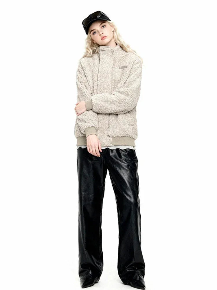 Woman wearing a cream-colored sherpa fleece bomber jacket, black faux leather pants, and a black baseball cap, standing with arms crossed.