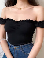 Woman wearing a black ribbed knit off-the-shoulder top with ruffled trim.