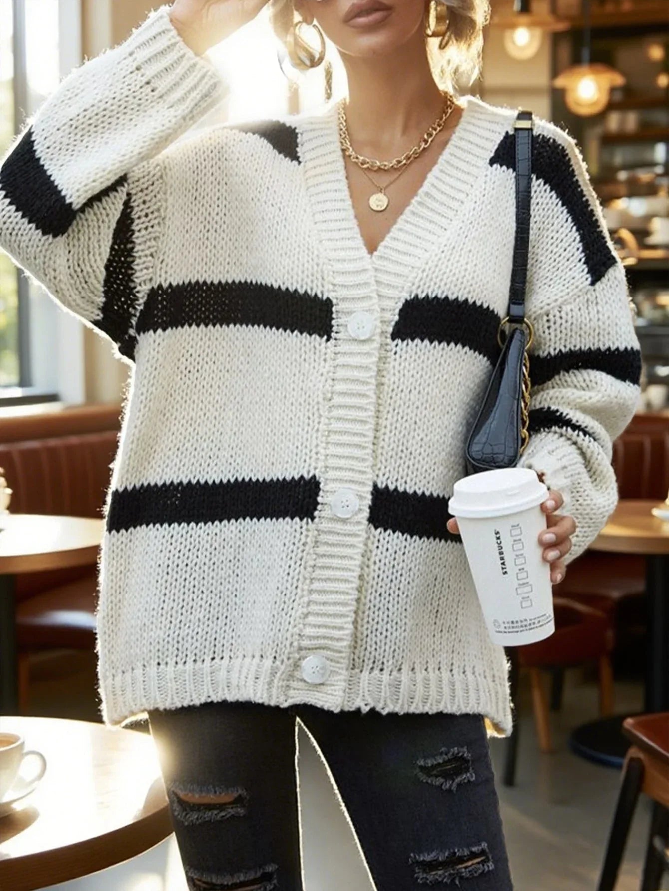 Close-up of a woman in a white and black striped knit cardigan, holding a coffee cup.