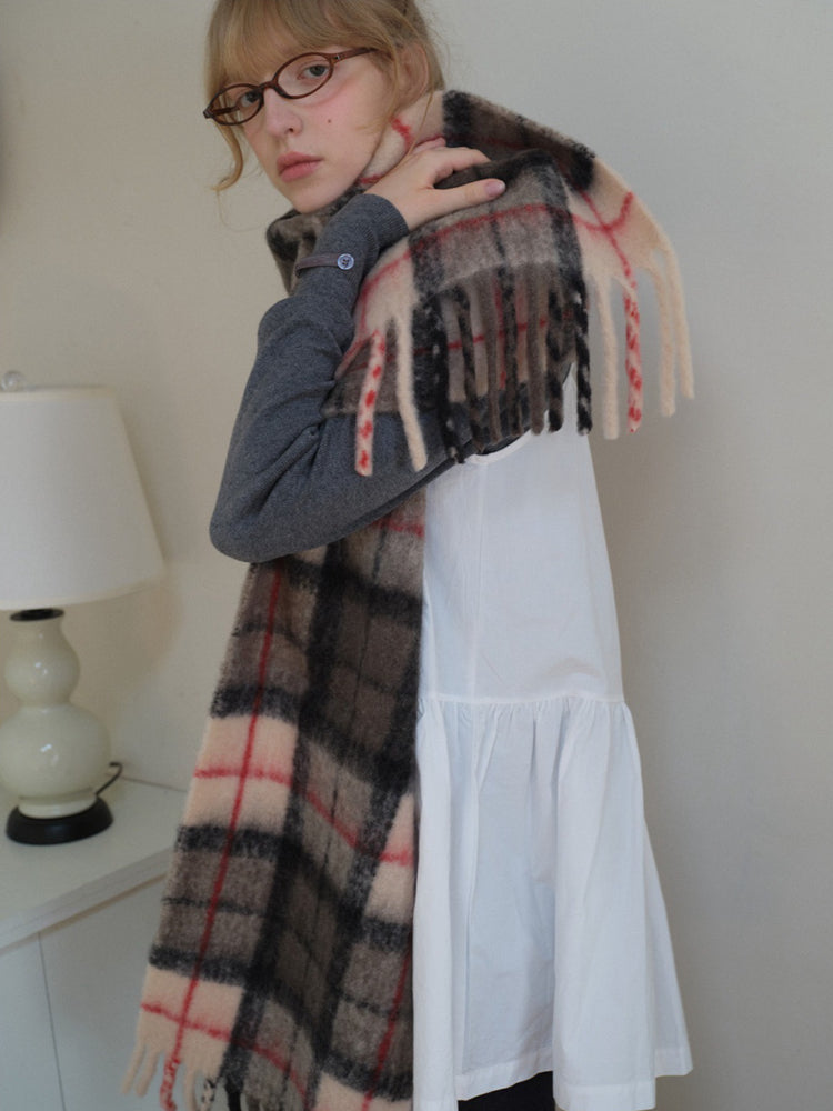 Woman in a white dress and grey sweater, adjusting a large plaid scarf.