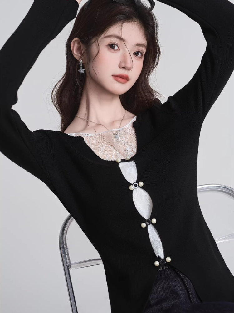 Woman wearing a black long-sleeved top with white lace trim and decorative buttons, posing with hands raised.
