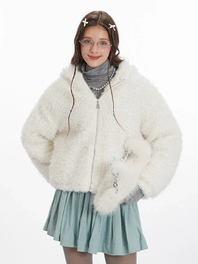 Close-up front view of a model wearing a white fuzzy hooded jacket with bunny ears, a grey turtleneck, and a light blue pleated skirt. She is wearing glasses and has hair clips.