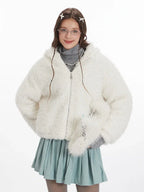 Close-up front view of a model wearing a white fuzzy hooded jacket with bunny ears, a grey turtleneck, and a light blue pleated skirt. She is wearing glasses and has hair clips.