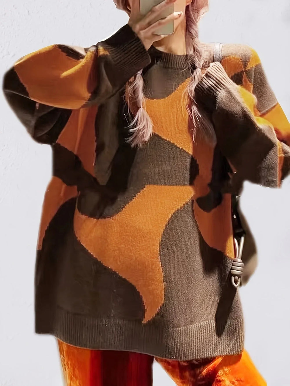 Close-up of a woman wearing a brown and orange abstract patterned oversized sweater with pink braided hair.
