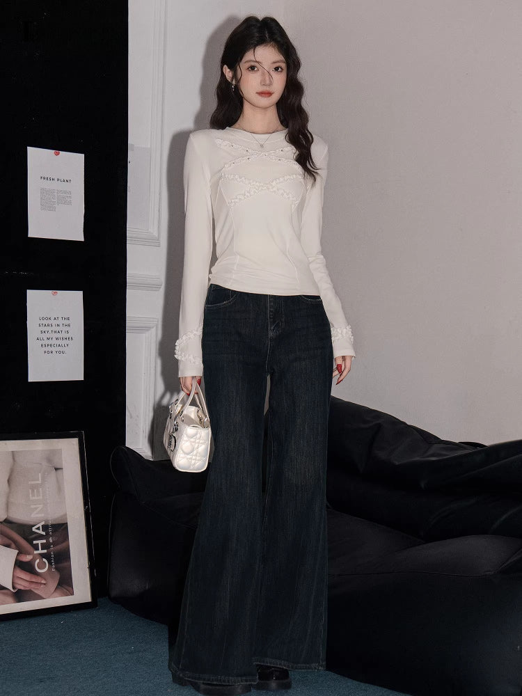 Full body shot of a woman in a white long-sleeved top with ruffled trim and dark wash wide-leg jeans, holding a white handbag.
