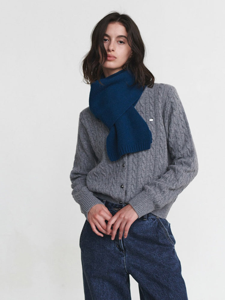 A woman wearing a grey cable-knit cardigan and a blue scarf.