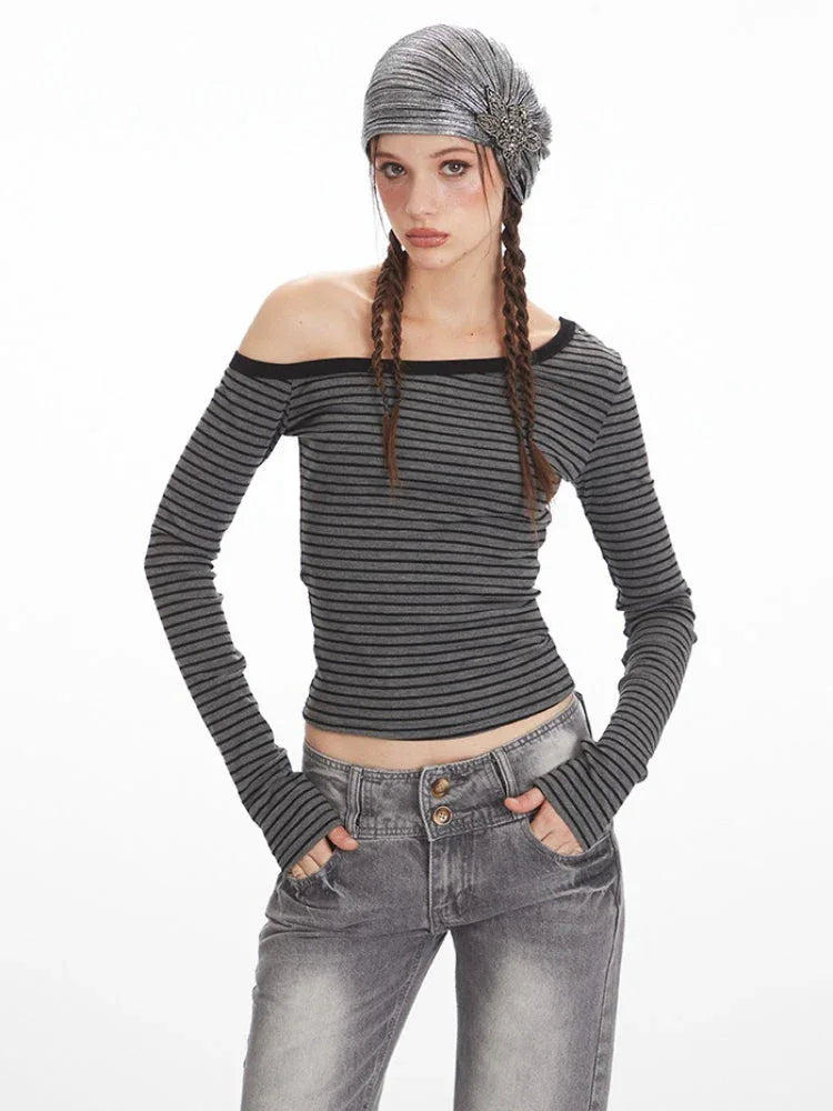 Close-up front view of a woman wearing a grey and black striped off-the-shoulder long-sleeve top and grey wide-leg jeans.