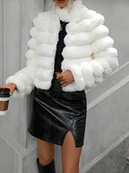 Woman holding a coffee cup while wearing a white faux fur cropped jacket, black top, and black skirt.