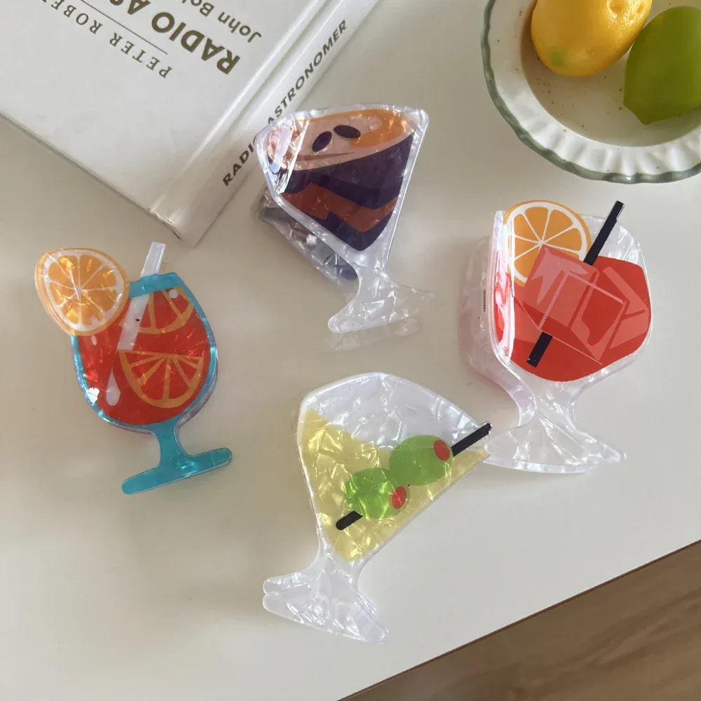 overhead view of four acrylic cocktail hair clips arranged on a white surface with books and fruit