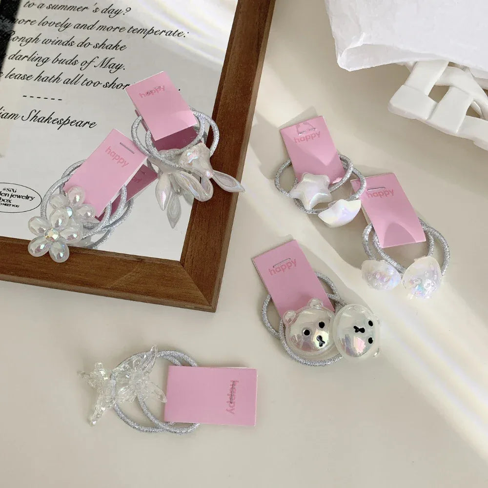 A collection of cute hair ties with various charms like flowers, stars, and bear faces, displayed on a white surface.