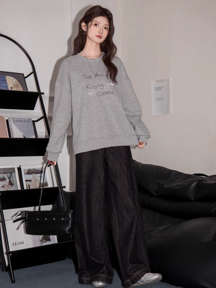 Full body shot of a woman wearing a grey crew neck sweatshirt with graphic print and black wide-leg jeans