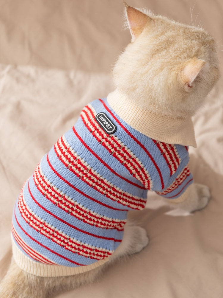 A white cat wearing a blue and red striped knit sweater, viewed from the back, showing the 'HIPIPET' tag.