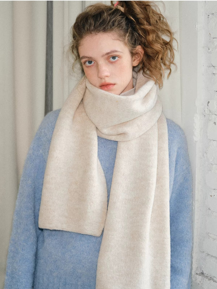 Model in a light blue knit sweater and a cream scarf, looking forward.