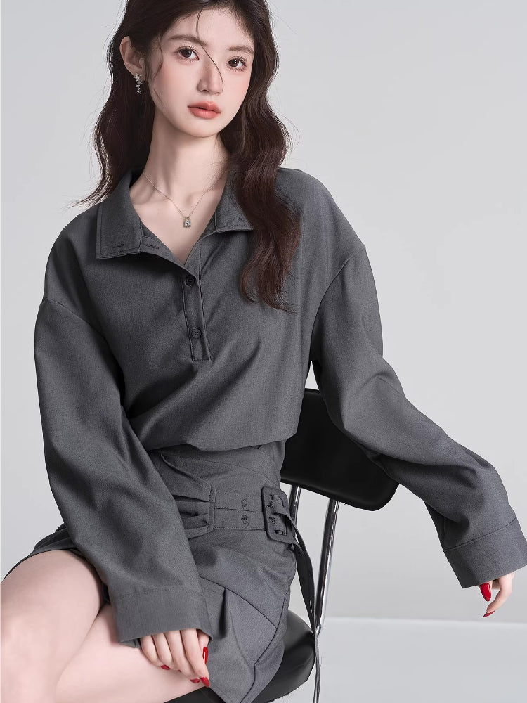 Model wearing a grey long-sleeved collared shirt and a grey asymmetrical skirt with pleats.